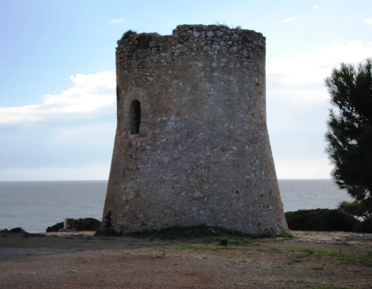 Historic stone coastal defense tower Torre de Cala Pi perched on cliffs above the sea inlet