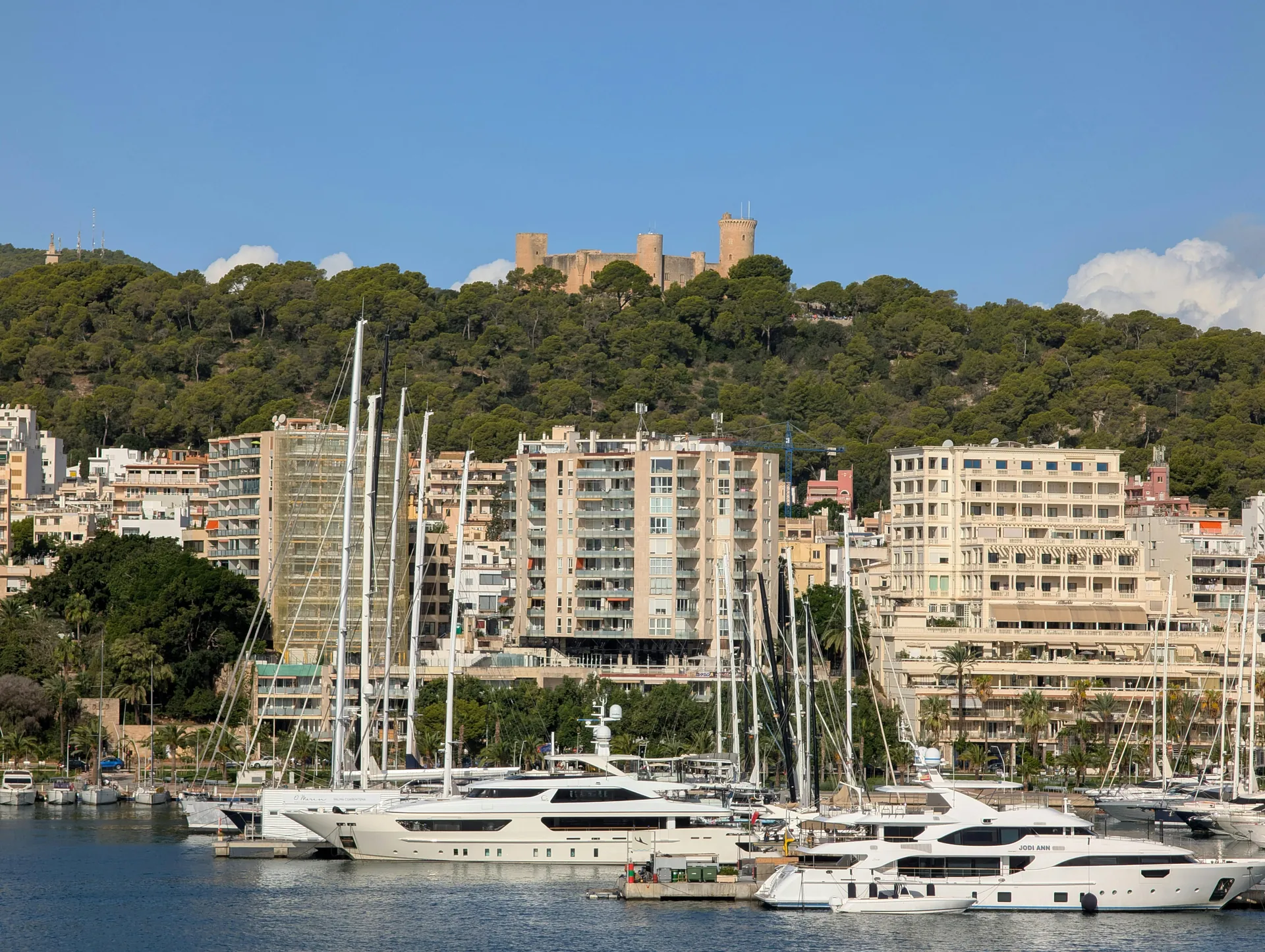 Explore the vibrant harbor of Palma, featuring luxurious yachts and the iconic Bellver Castle in the distance.